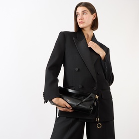 Model carrying Alaia Le Click Medium Shoulder Bag in noir smooth leather, gold-tone hardware, worn crossbody with black tailored blazer and trousers