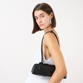 Model carrying Alaia Le Teckel Small Shoulder Bag in noir textured leather, silver-tone hardware, tubular strap, elongated silhouette
