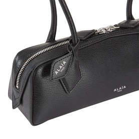 Alaia Noir leather shoulder bag, close-up showing silver zip detail, dual top handles and embossed logo patch.