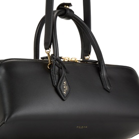 Alaia noir calf leather tote bag, close-up of gold-tone zip hardware and branded leaf charm detail on double top handles.