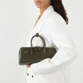 Model carrying Alaia Delta Small Tote Bag in Vert Camouflage nubuck calfskin, gold-tone hardware, top handle, styled with white blazer