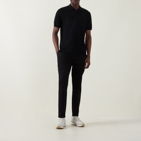 Model wearing Arne Tailored Slim-Leg Chinos in black, styled with a black polo shirt and white trainers.