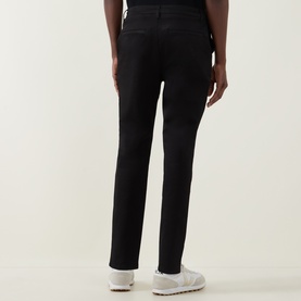 Model wearing Arne Tailored Slim-Leg Chinos in black, slim fit with clean hems, styled with white trainers, rear view.