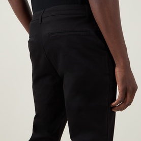 Model wearing Arne Tailored Slim-Leg Chinos in black, showing rear jetted pockets and slim fit stretch fabric from behind.