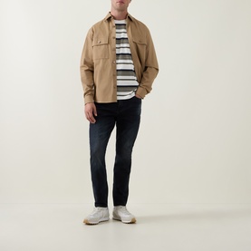 Model wearing Arne Slim-Leg Jeans in Midnight Blue, dark wash denim, styled with a sand overshirt and striped tee.