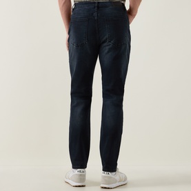 Model wearing Arne Slim-Leg Jeans in Midnight Blue, dark wash stretch denim, slim fit, styled with white trainers
