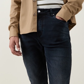 Model wearing Arne Slim-Leg Jeans in Midnight Blue dark wash stretch denim, styled with a camel jacket and striped top.