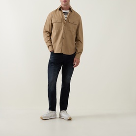 Model wearing Arne Slim-Leg Jeans in Midnight Blue, dark wash denim, styled with a beige overshirt and white trainers.