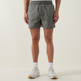 Model wearing Arne sage swim shorts with elasticated drawstring waist, styled with white socks and cream trainers.