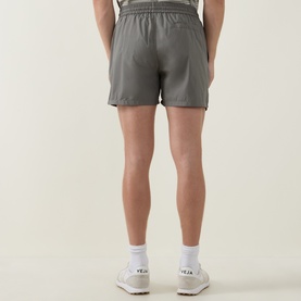 Model wearing Arne sage swim shorts, back view, styled with white Veja trainers and white socks