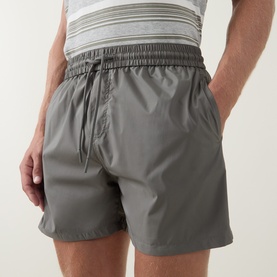 Model wearing Arne sage swim shorts with elasticated drawstring waist and side pockets, styled with a striped white T-shirt.