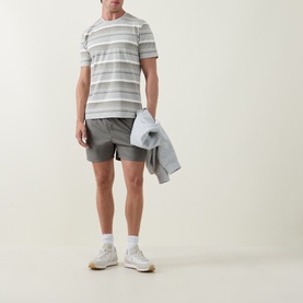 Model wearing Arne Sage swim shorts with a grey striped t-shirt and white socks with trainers, carrying a light grey jacket.