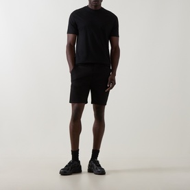 Model wearing Arne Tailored Slim-Leg Chino Shorts in black, styled with a black T-shirt and black chunky trainers.