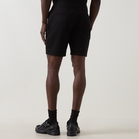 Model wearing Arne Tailored Slim-Leg Chino Shorts in black, knee-length with slim fit, styled with black trainers and socks, rear view.