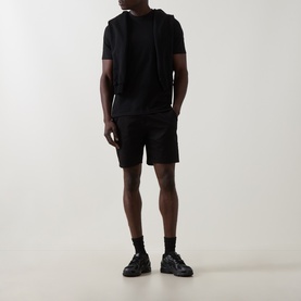 Model wearing Arne Tailored Slim-Leg Chino Shorts in black, styled with a black hoodie and black trainers.