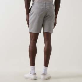 Model wearing Arne stone cotton shorts, rear view, styled with white socks and trainers.