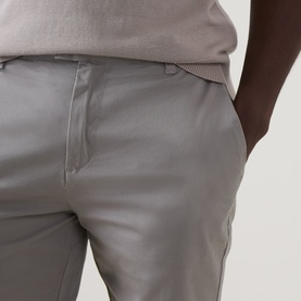Model wearing Arne stone cotton shorts, close-up of waistband and front pocket detail, styled with a light grey knit top
