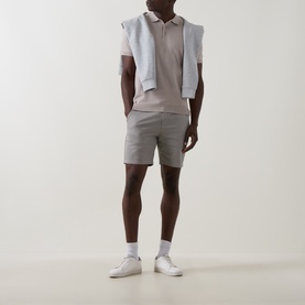 Model wearing Arne stone cotton shorts, styled with a mauve polo shirt, grey knit vest and white trainers.