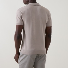 Model wearing Arne Stone knit polo shirt, back view, styled with light grey trousers.