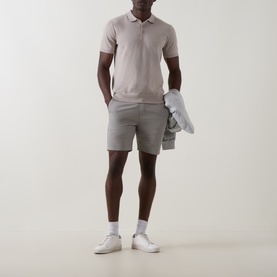 Model wearing Arne stone knit polo shirt, styled with grey shorts and white trainers, holding a light grey jacket.