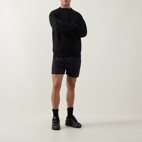 Model wearing Arne Essential Drawstring Swim Shorts in black, styled with a black sweatshirt and chunky black trainers.