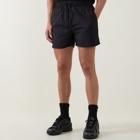 Model wearing Arne Essential Drawstring Swim Shorts in black, paired with black socks and chunky trainers.