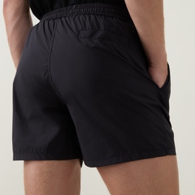 Model wearing Arne Essential Drawstring Swim Shorts in black, rear view showing elasticated waistband and rear welt pocket with popper closure.