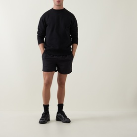 Model wearing Arne Essential Drawstring Swim Shorts in black, styled with matching black sweatshirt and black chunky trainers.