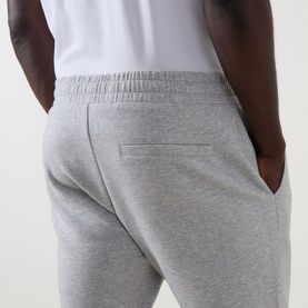Model wearing Arne Essential Slim-Leg Sweatpants in Marl Grey, showing rear welt pocket and elasticated waistband detail, styled with white tee.