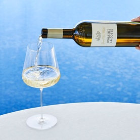Chateau La Coste Grand Vin Blanc 1.5L white wine being poured into a large wine glass, set against a blue background
