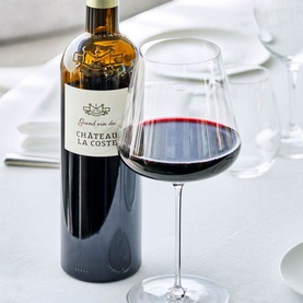 Chateau La Coste Grand Vin Rouge 1.5L red wine bottle alongside a filled balloon wine glass on a white table
