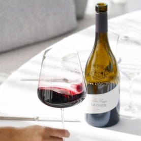 Chateau La Coste Le Rouge 500ml red wine bottle beside a filled wine glass on a white dining table