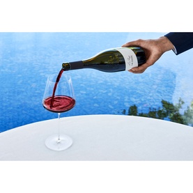 Chateau La Coste Le Rouge 500ml red wine being poured into a large stemmed glass on a white table, poolside setting
