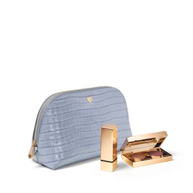 Aspinal of London Sky Blue croc-embossed makeup bag with gold zip, styled with a gold lipstick case and open eyeshadow palette.