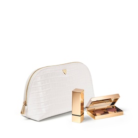 Aspinal of London Chalk White croc-embossed cosmetic case with gold-zip trim, styled with a gold lipstick and eyeshadow palette.