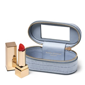 Aspinal of London Sky Blue croc-embossed oval lipstick case with mirror lid, shown open alongside two gold-cased red lipsticks.