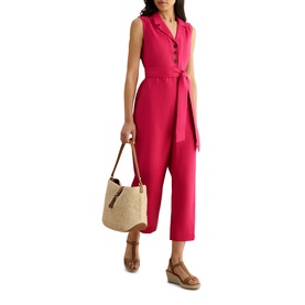Model wearing Hobbs cherry pink sleeveless belted jumpsuit with lapel collar, styled with a raffia tote bag and tan wedge sandals.