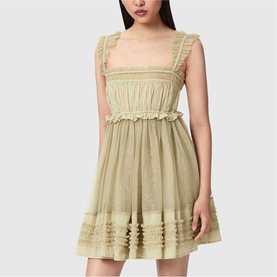 Model wearing sage green sleeveless mini dress with ruffle trim, smocked bodice, and flared skirt