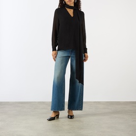 Model wearing House of Dagmar black wool blouse with draped neckline tie, styled with wide-leg blue jeans and black mules