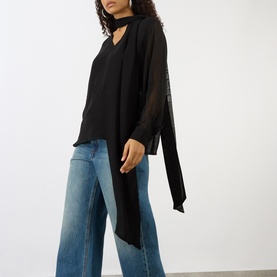 Model wearing House of Dagmar black wool blouse with draped neckline tie, sheer sleeves, and asymmetric hem, styled with blue wide-leg jeans.