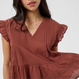 Model wearing Kaffe dress in Henna, featuring V-neckline, ruffle cap sleeves, pintuck detail and tiered skirt