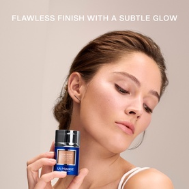 Model with La Prairie Skin Caviar Concealer Foundation SPF 30 in Soft Pearl, holding the dark blue bottle, showcasing a luminous, glowing complexion.