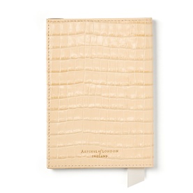 Aspinal of London passport cover in buttermilk croc-embossed leather with gold foil branding and cream grosgrain ribbon detail.