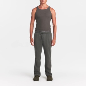 Model wearing Skims dark brown lounge trousers with elasticated logo waistband, styled with matching tank top and khaki slippers