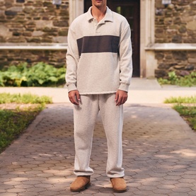 Model wearing Skims Rugby Polo Shirt in Light Heather Grey with contrast chest stripe, styled with matching grey joggers and tan suede shoes.