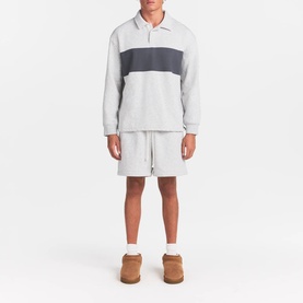 Model wearing Skims light heather grey colourblock polo sweatshirt, styled with matching shorts and tan shearling slippers.