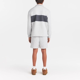 Model wearing Skims light heather grey colour-block pullover top, styled with matching shorts and tan trainers, seen from behind.