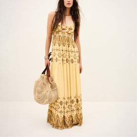 Model wearing Bash yellow sleeveless maxi dress with gold embroidered print, styled with a round woven bag