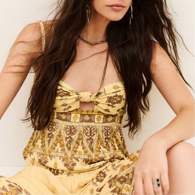 Model wearing Bash yellow floral printed bustier top with bow detail, styled with matching wide-leg trousers and layered necklaces