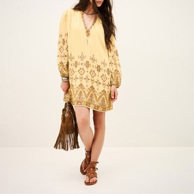 Model wearing Bash yellow embroidered mini dress with V-neckline and long sleeves, styled with tan gladiator sandals and brown fringe bag